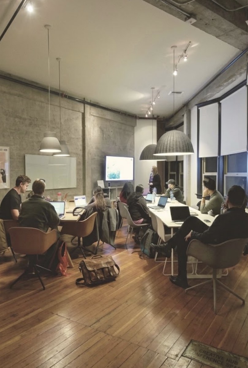 Gruppe mit Laptops in einem Loft-Buero, vorn eine Praesentation an der Wand
